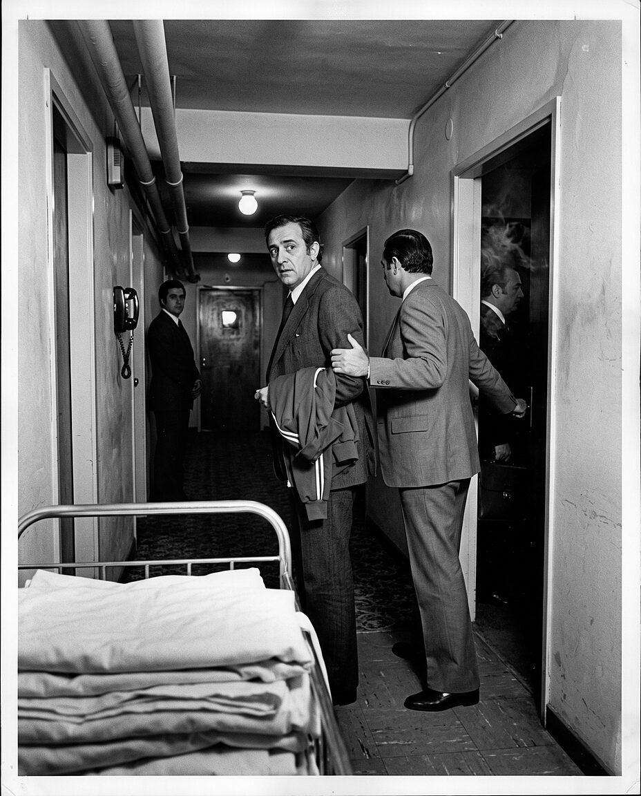 A head coach is escorted along a hotel corridor by officials in suits, seventy-five minutes before a national final in 1978
